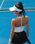Woman on a tennis court wearing a white visor and black skirt.