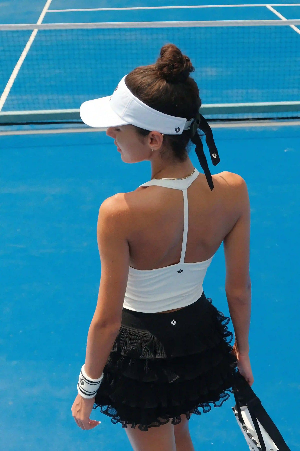 Woman on a tennis court wearing a white visor and black skirt.