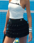Tennis player on a court wearing a white top and black skirt with a visor.