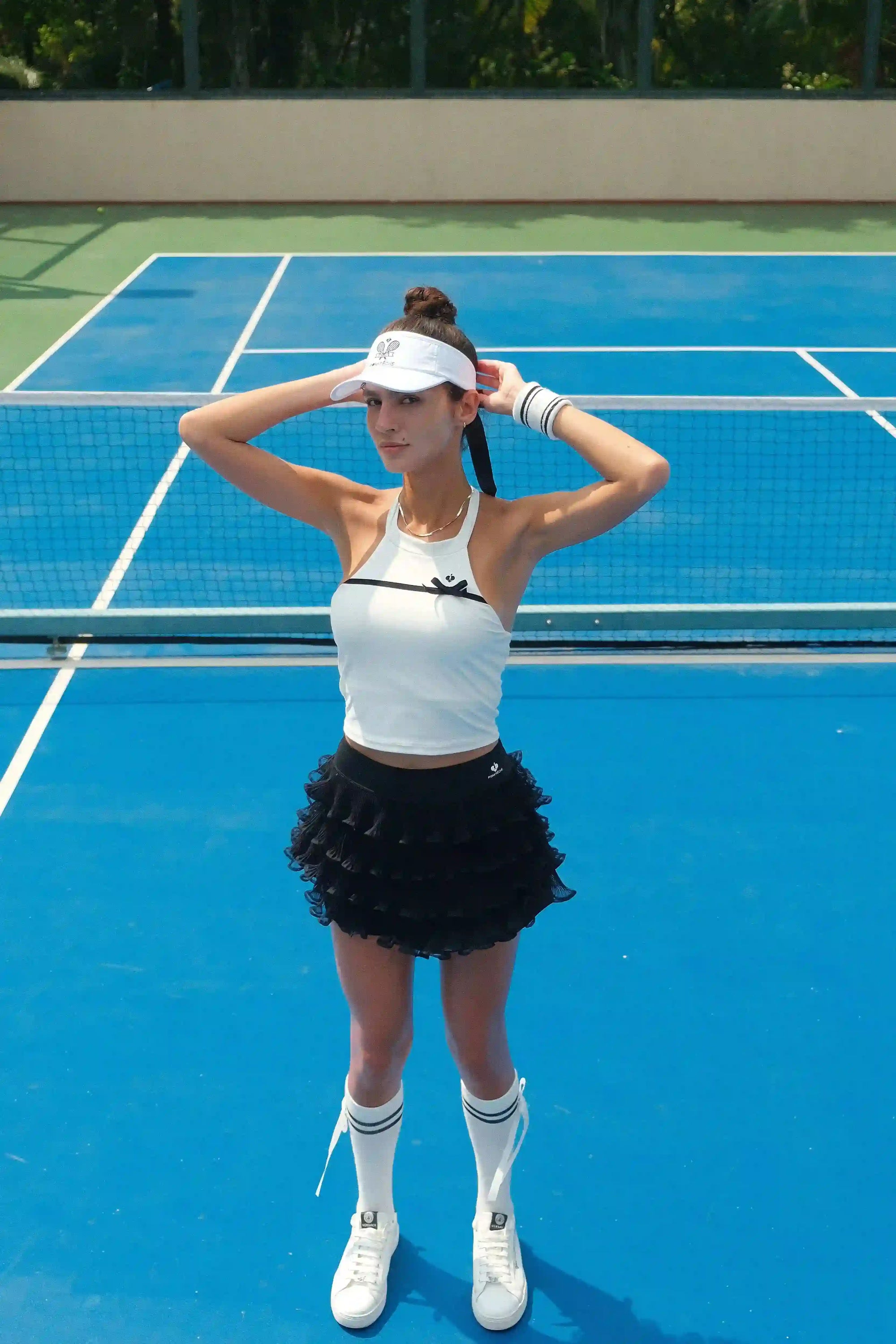 Woman on a tennis court wearing a white top, black skirt, and white visor.