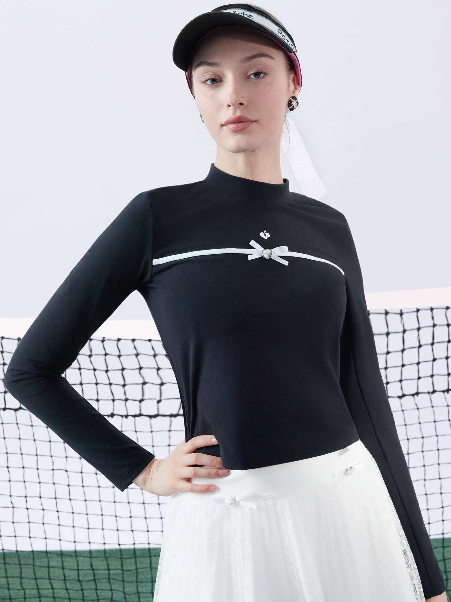 Black long-sleeve top with a smooth silhouette and contrast bow detail, styled on the tennis court.