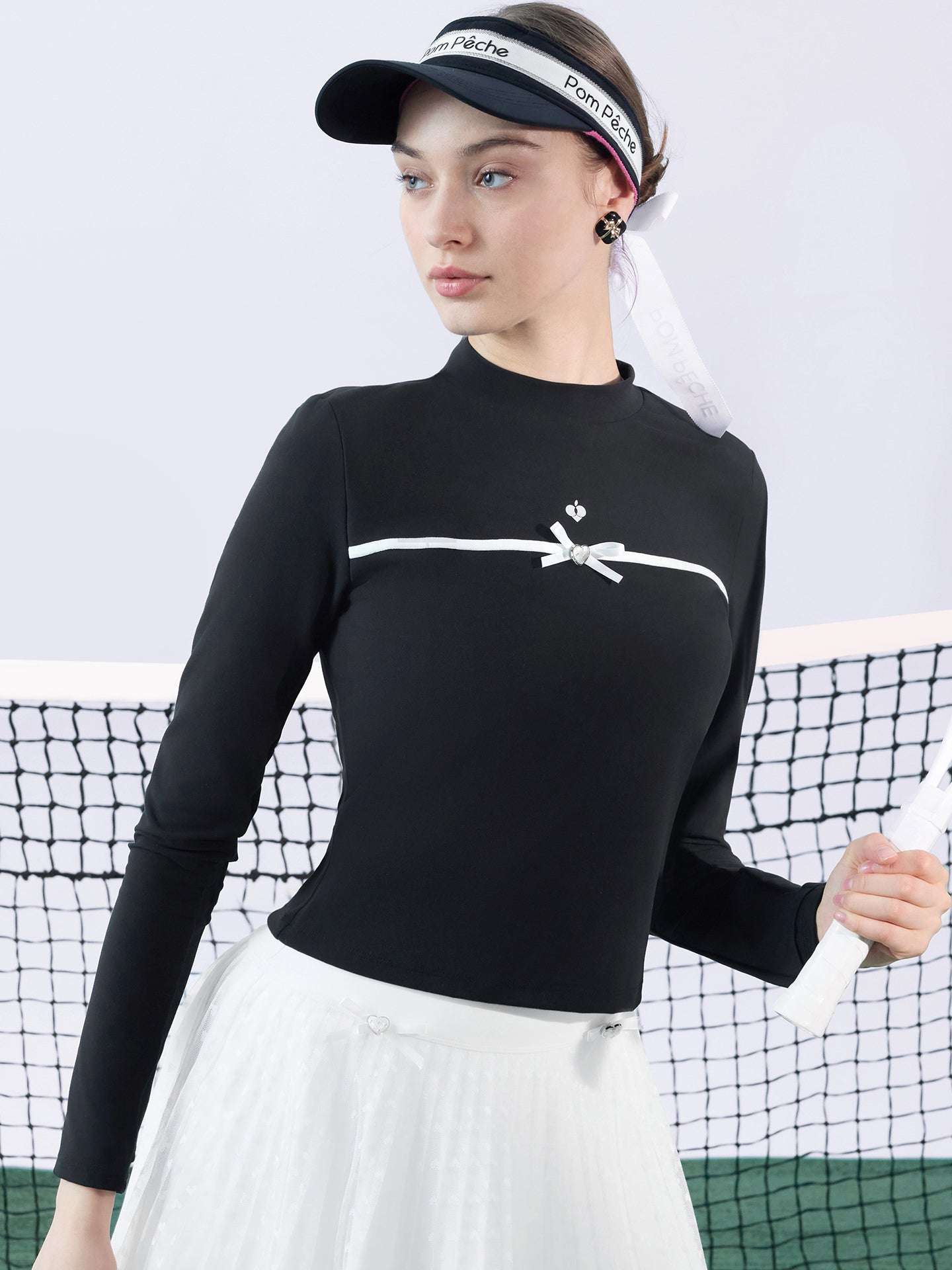 Black long-sleeve top with a smooth silhouette and contrast bow detail, styled on the tennis court.