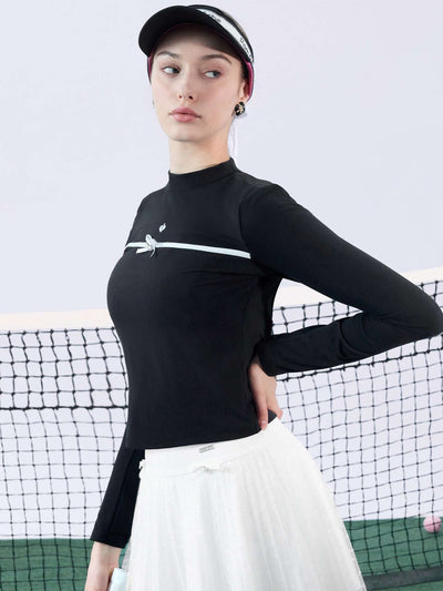 Black long-sleeve top with a smooth silhouette and contrast bow detail, styled on the tennis court.