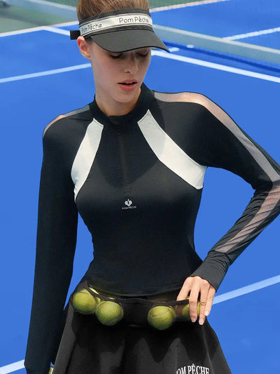 Black long-sleeve fitted top with a half-zip neckline and subtle logo detail, styled on the tennis court