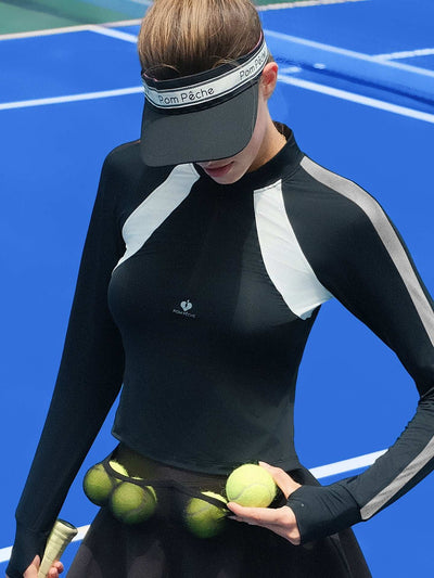 Black long-sleeve fitted top with a half-zip neckline and subtle logo detail, styled on the tennis court.