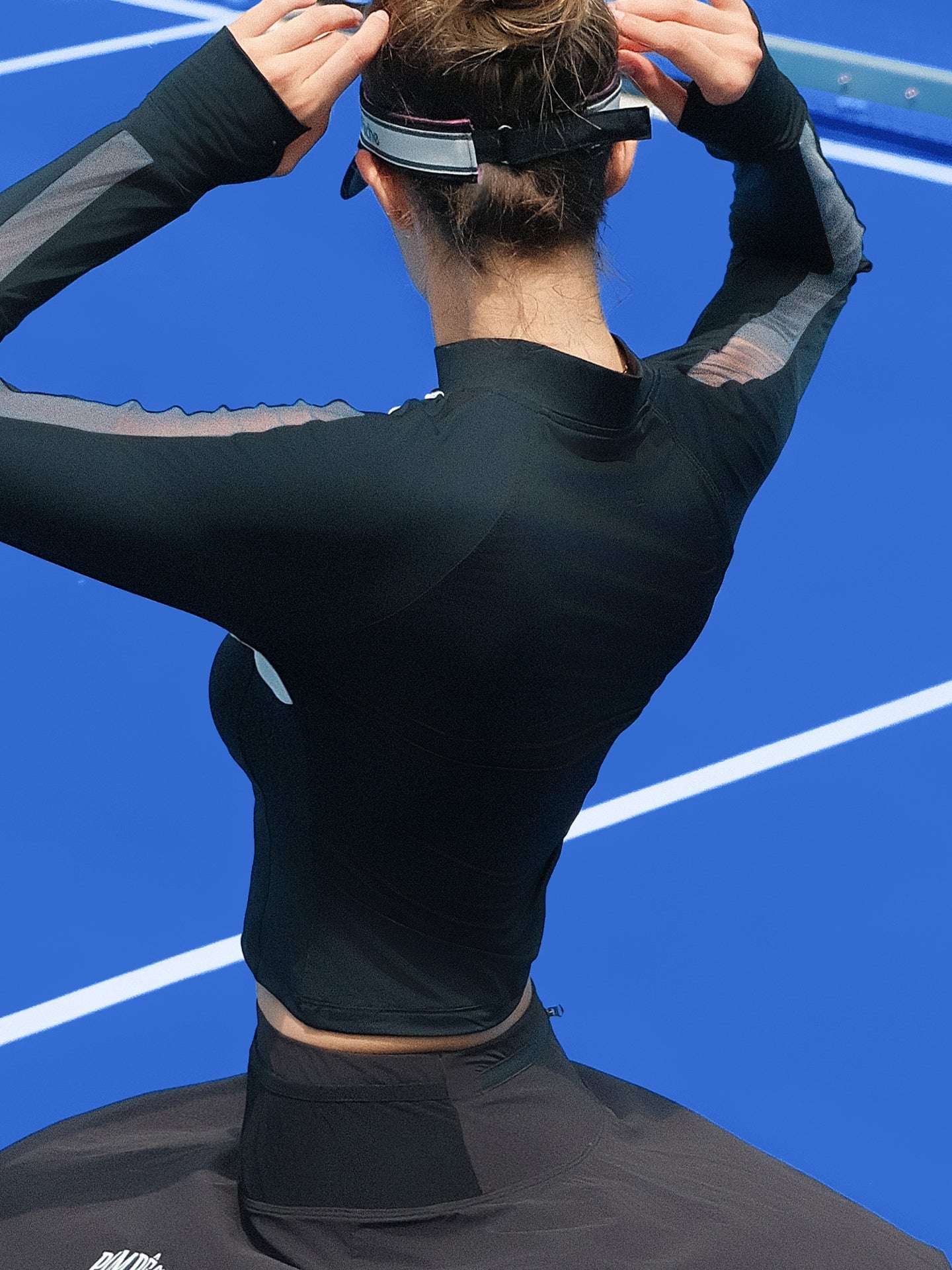 Black long-sleeve fitted top with a half-zip neckline and subtle logo detail, styled on the tennis court.