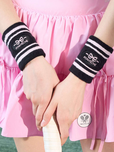 Black tennis wristbands with soft pink stripes, featuring embroidered bow and logo details.
