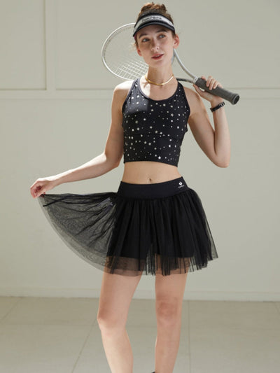 Model wearing a black tulle puff tennis skirt with star-print top, showing airy layered mesh and a high-waisted athletic tennis skirt silhouette.