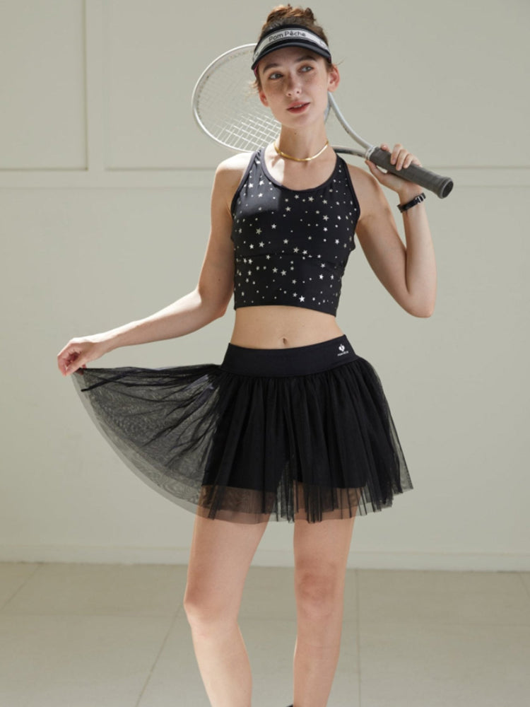 Model wearing a black tulle puff tennis skirt with star-print top, showing airy layered mesh and a high-waisted athletic tennis skirt silhouette.
