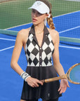 Black and white checkered tennis dress with a V-neck, flared skirt, and sleeveless design, styled on a tennis court.