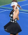 Black and white checkered tennis dress with a V-neck, flared skirt, and sleeveless design, styled on a tennis court.