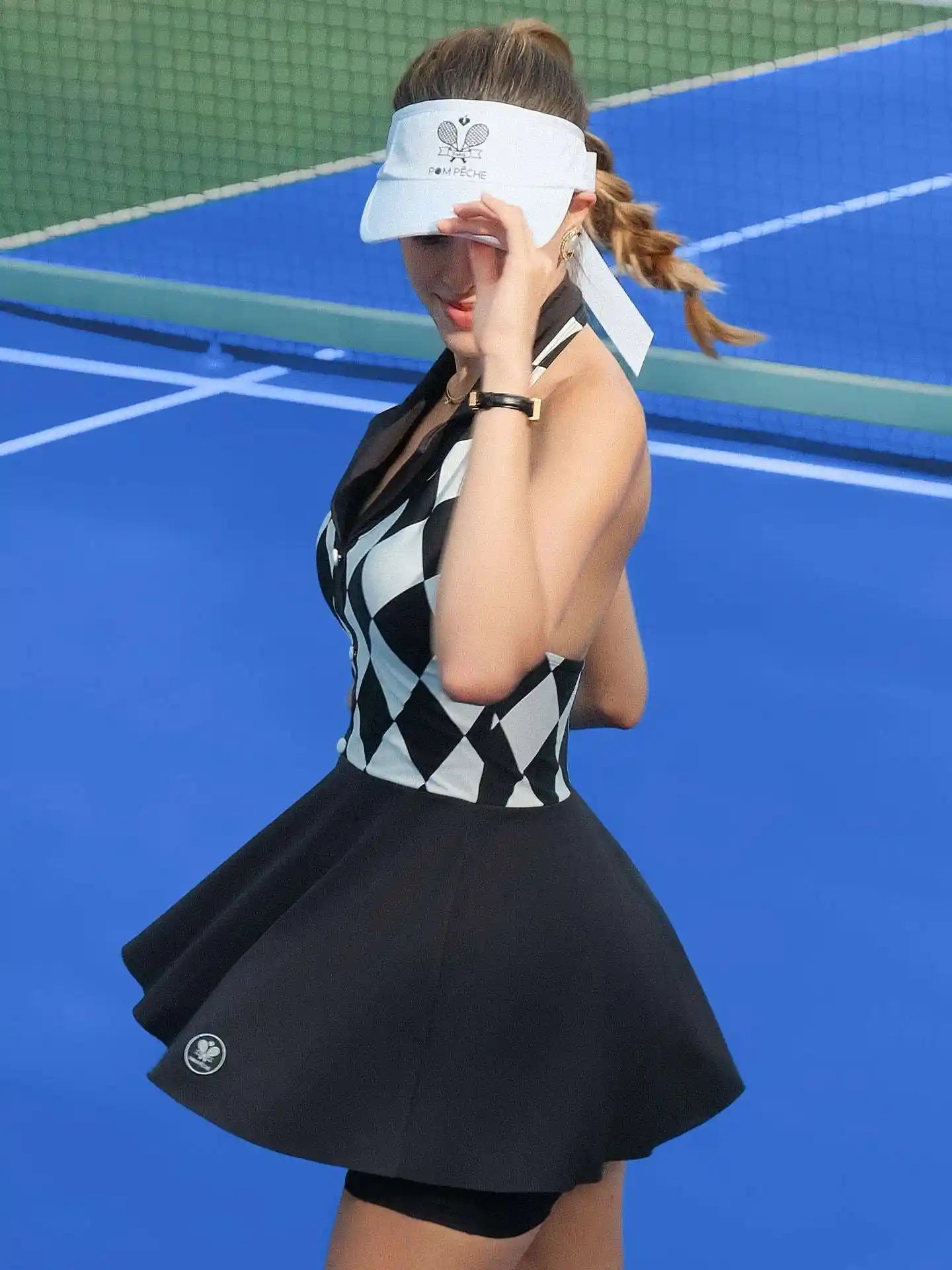 Black and white checkered tennis dress with a V-neck, flared skirt, and sleeveless design, styled on a tennis court.