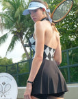 Black and white checkered tennis dress with a V-neck, flared skirt, and sleeveless design, styled on a tennis court.