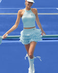 Light blue halter neck crop top with bow detail and subtle logo, styled on the tennis court.