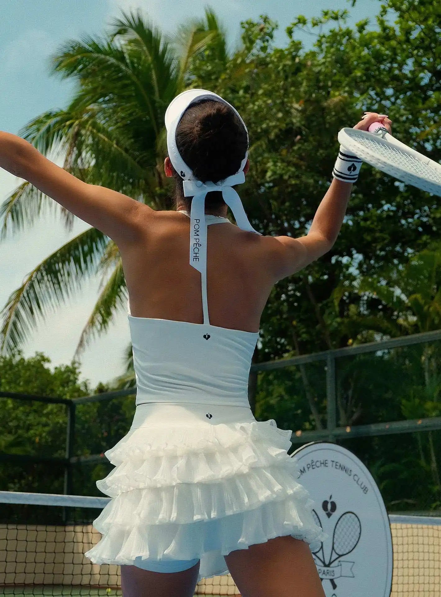 Light blue halter neck crop top with bow detail and subtle logo, styled on the tennis court.