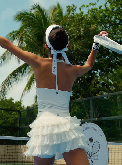 Light blue halter neck crop top with bow detail and subtle logo, styled on the tennis court.