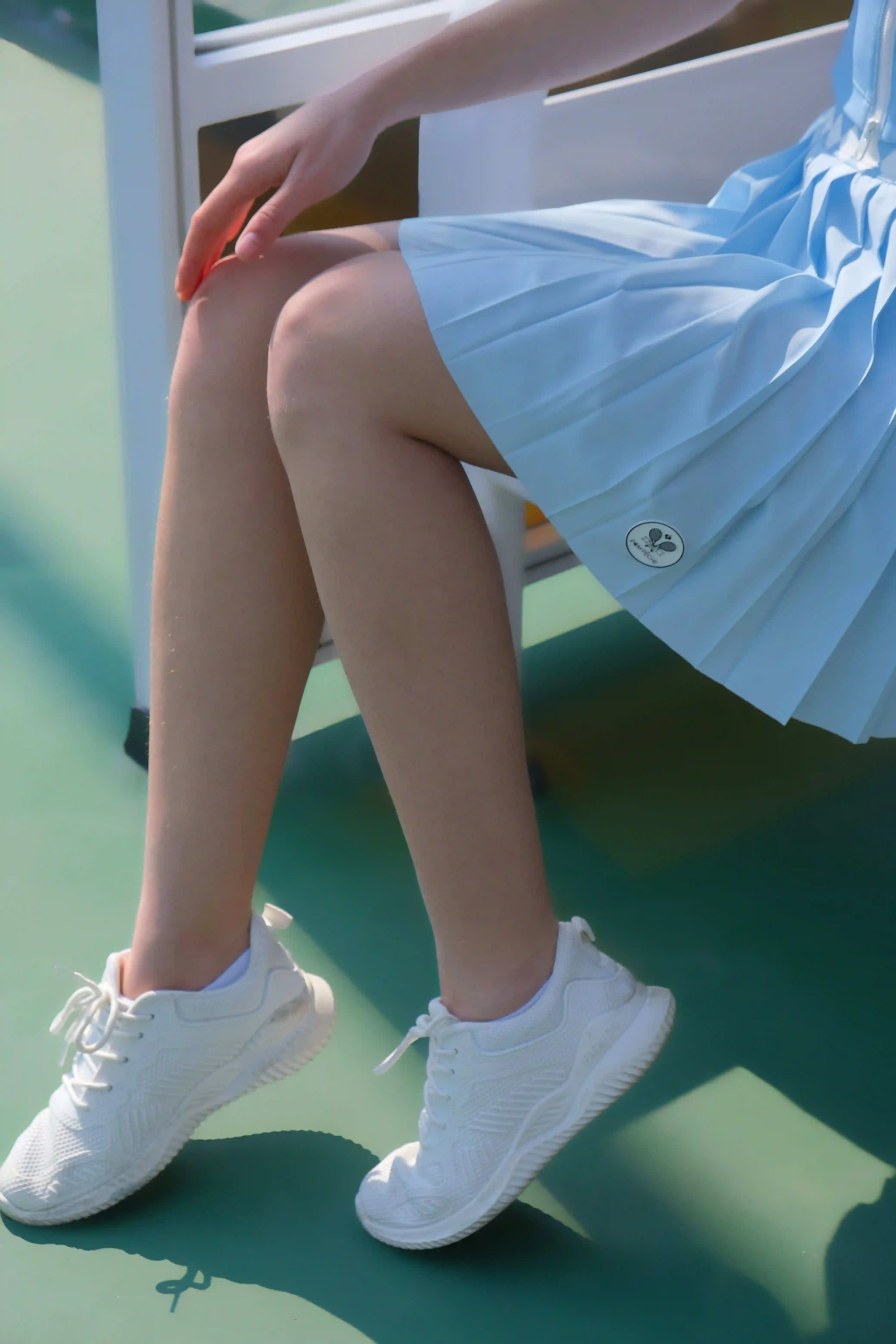 Person wearing white sneakers and a light blue dress sitting on a green floor.