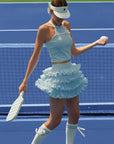 Woman in light blue tennis outfit with skirt on a tennis court