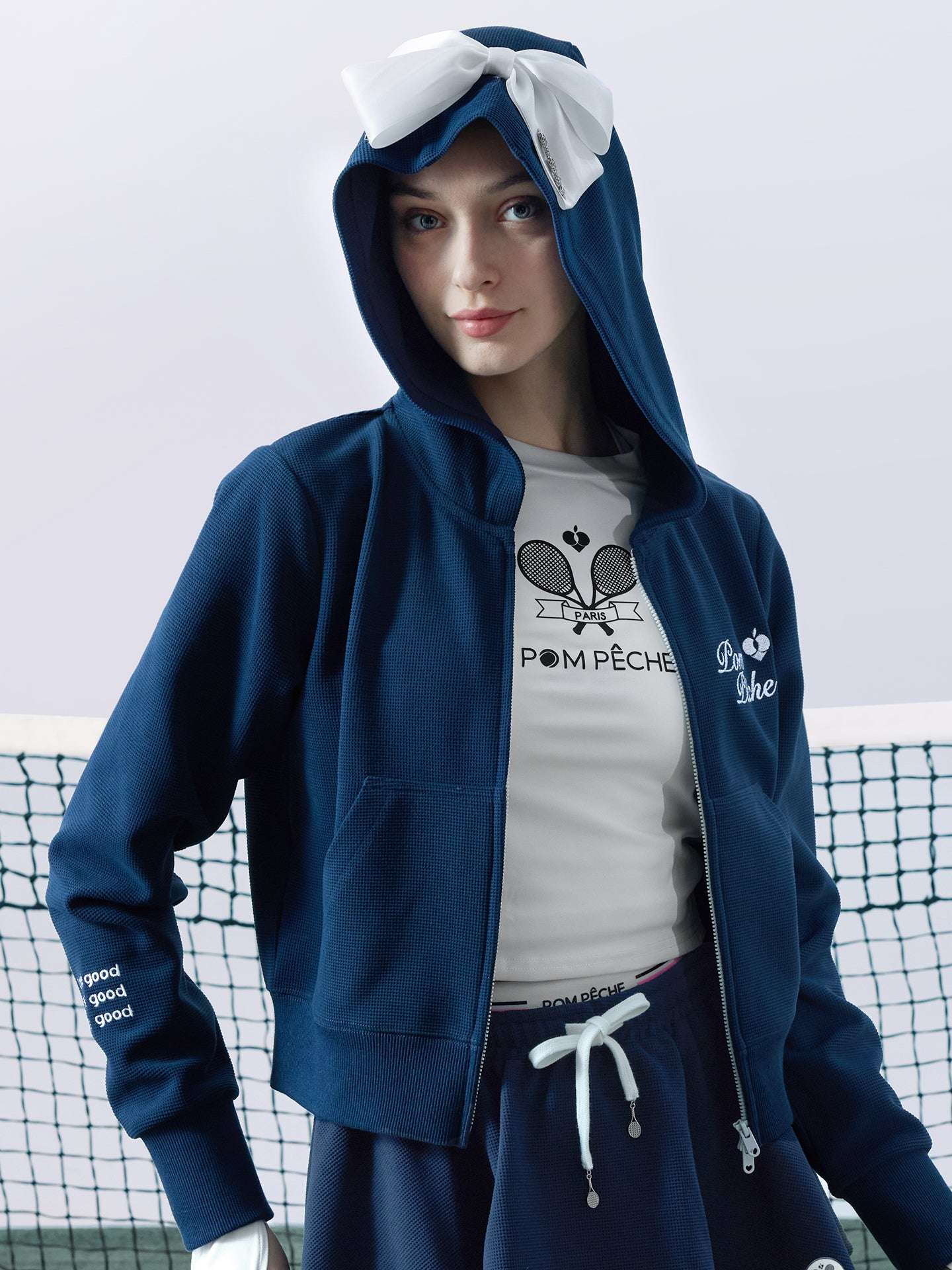 Navy blue zip-up hoodie with bow detail on the hood and embroidered logo, perfect for warm-ups or everyday wear.