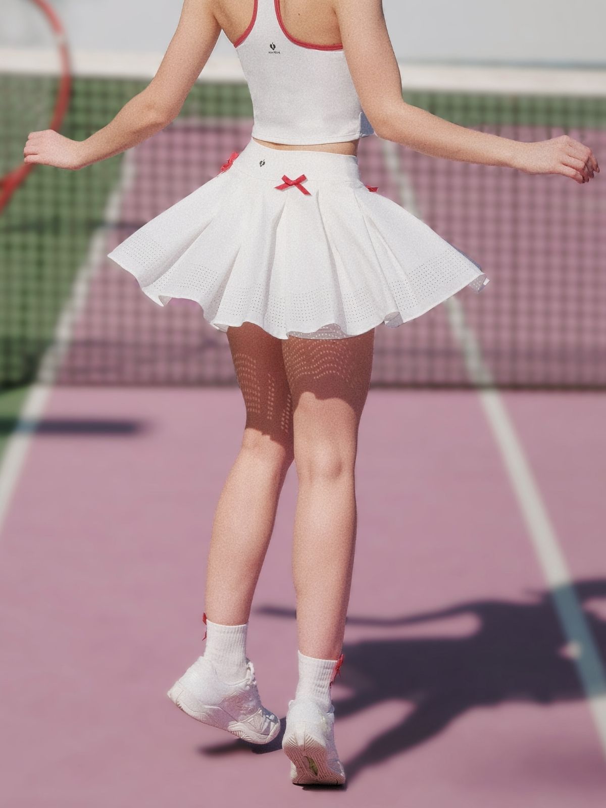Model twirling in the Bow-Heart Pleated Skirt – Paris White, showing red bow and flowing pleats.
