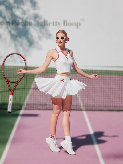 Woman in a tennis outfit with a skirt and top on a tennis court, holding a racket.