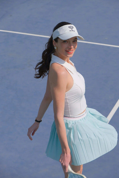 Woman on a tennis court wearing a white visor and light blue skirt.