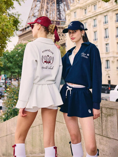 Two women in matching outfits with embroidered text, standing in front of the Eiffel Tower.