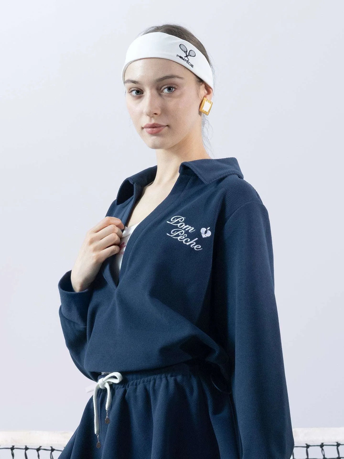 Woman wearing a navy blue tracksuit with 'L'ym Pche' branding, standing on a tennis court.