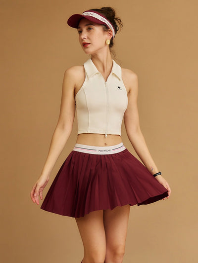 Woman wearing a beige sleeveless top and wine red skirt with visor against a brown background