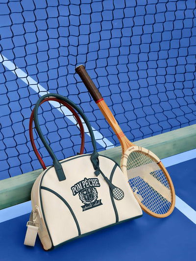 Cream dome tennis bag with contrast handles and Pom Pêche logo, styled on a tennis court.