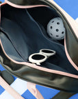 Cream dome tennis bag with contrast handles and Pom Pêche logo, styled on a tennis court.
