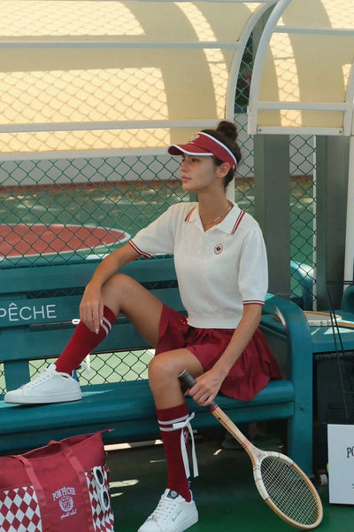 Woman sitting on a bench with a tennis racket, wearing a red and white outfit, in an outdoor setting.