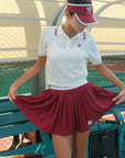 Person wearing a white polo shirt with red accents and a red skirt on a tennis court.