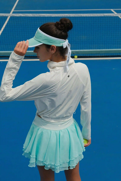 Tennis player on a court wearing a white shirt and light blue skirt.