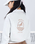Gray sweatshirt with quarter-zip design and embroidered logo, paired with a tulle skirt, styled on the tennis court for a chic, sporty look.