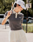 Outdoor rendering of a gray tennis top with puff sleeves worn by a model.