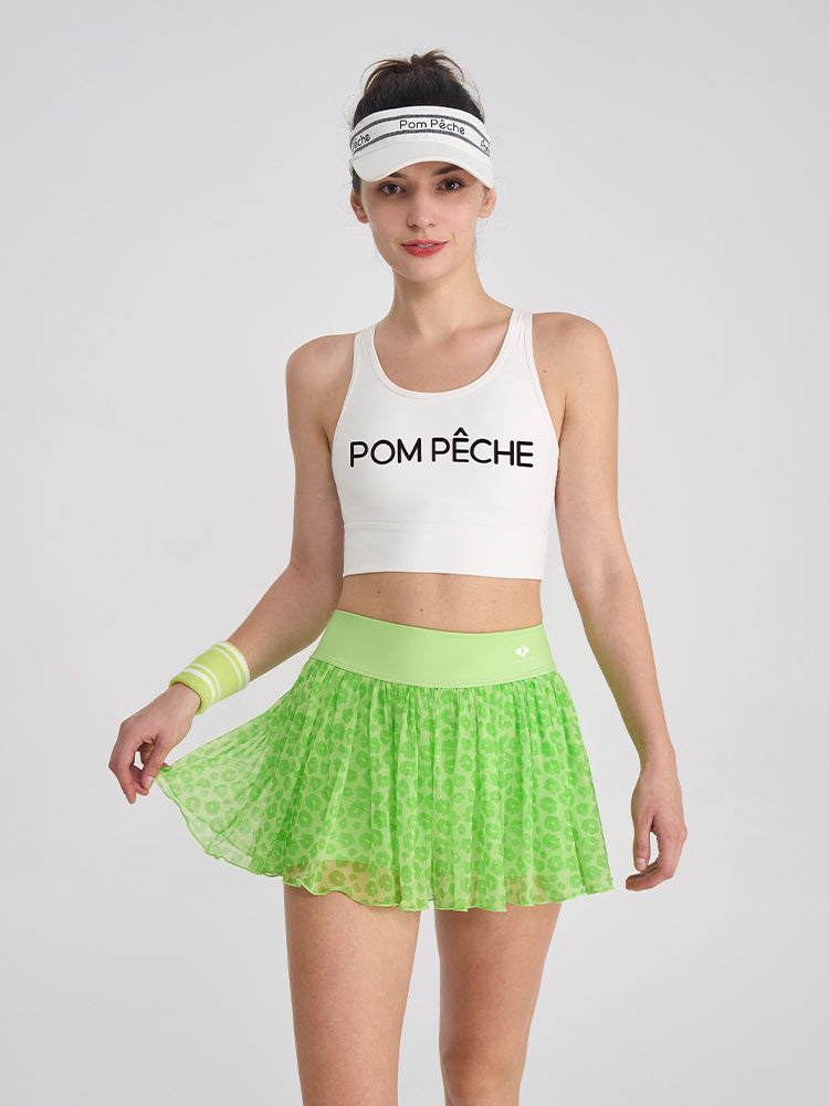 A model stands in a green leopard print tennis skirt with a stretchy waistband, showing breathable mesh perfect for tennis and pickleball.