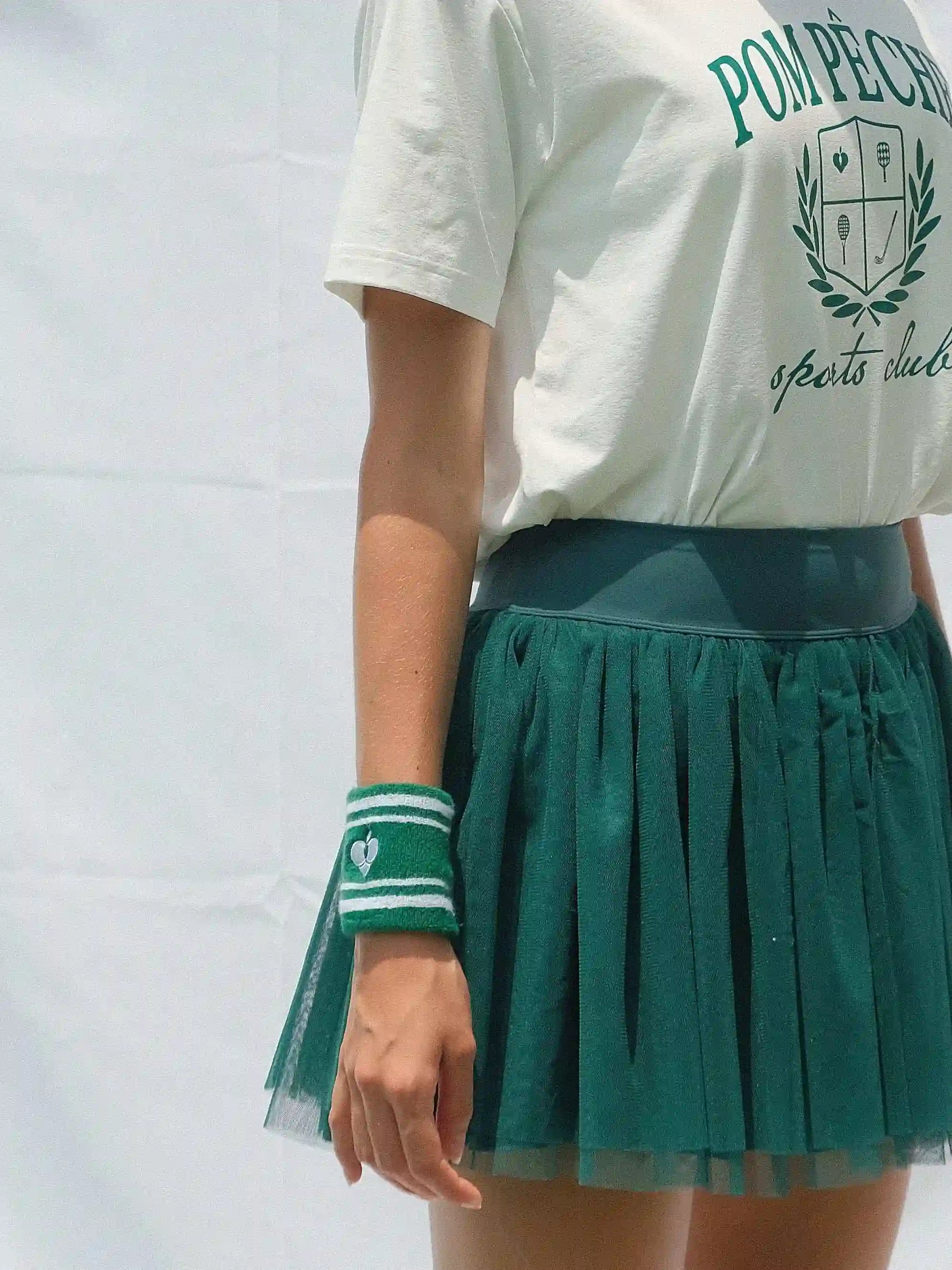 Person wearing a white t-shirt with 'Pompeii' text and a green pleated skirt on a plain background