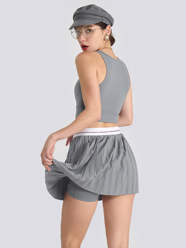 A grey women’s pleated tennis skirt with built-in shorts and a flexible waistband, offering comfort and style for active sports.