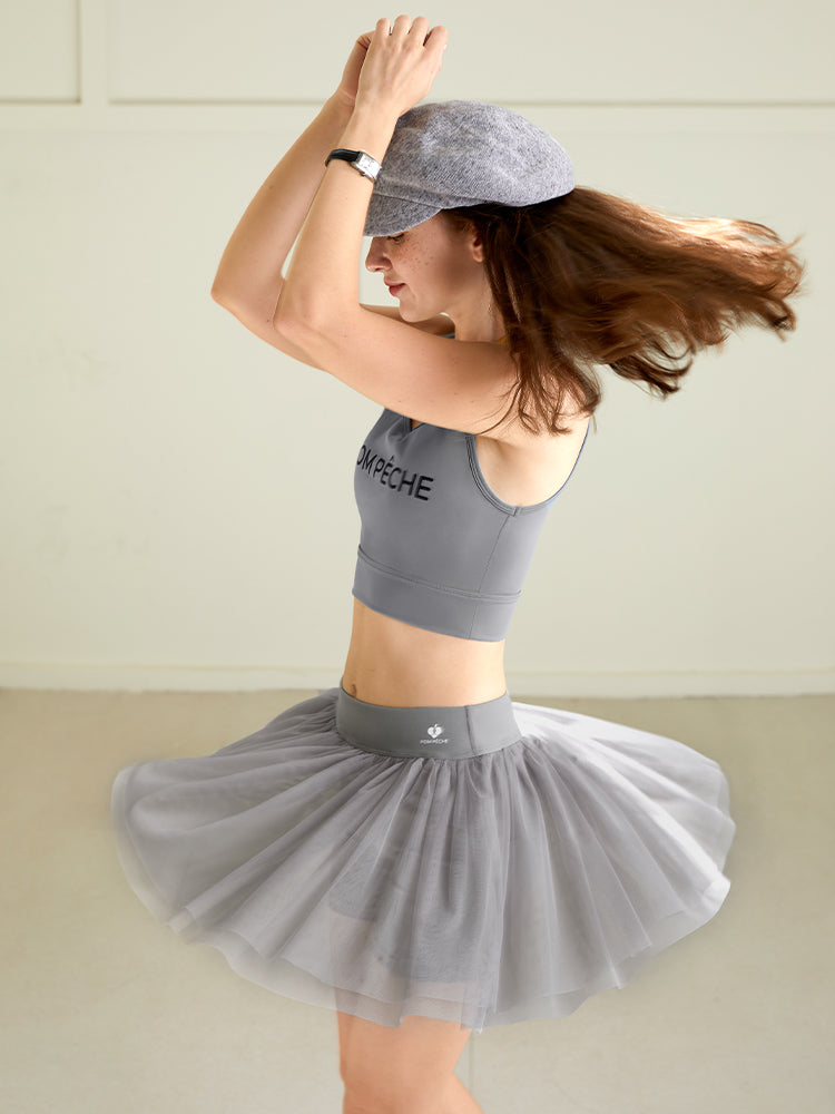 Model wearing a grey tulle puff tennis skirt in motion, showing airy layered mesh and a high-waisted athletic tennis skirt silhouette.