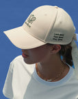 Ivory tennis baseball cap with embroidered Pom Pêche logo and detachable ribbon.