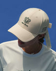 Ivory tennis baseball cap with embroidered Pom Pêche logo and detachable ribbon.