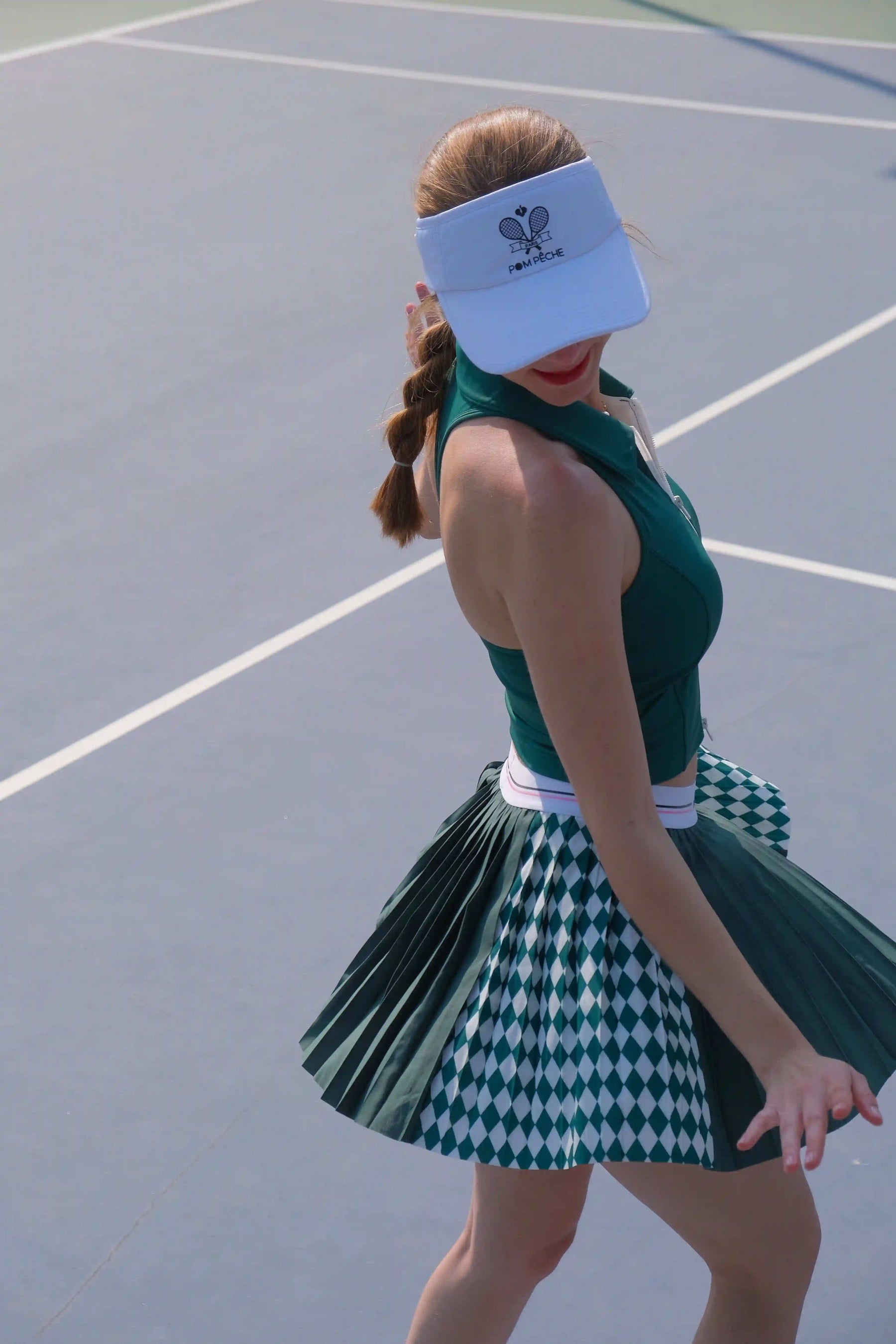 Person wearing a green tennis outfit with a visor on a tennis court