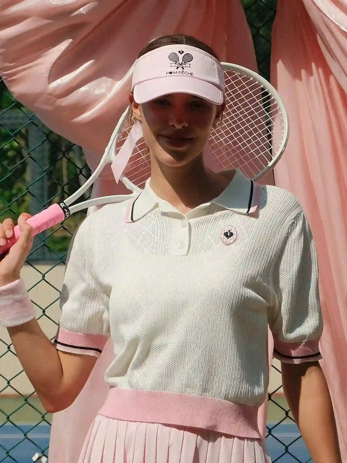 Person holding a pink tennis racket on a tennis court with pink fabric in the background