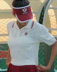Person wearing a white tennis top with red accents and a red visor on a tennis court.