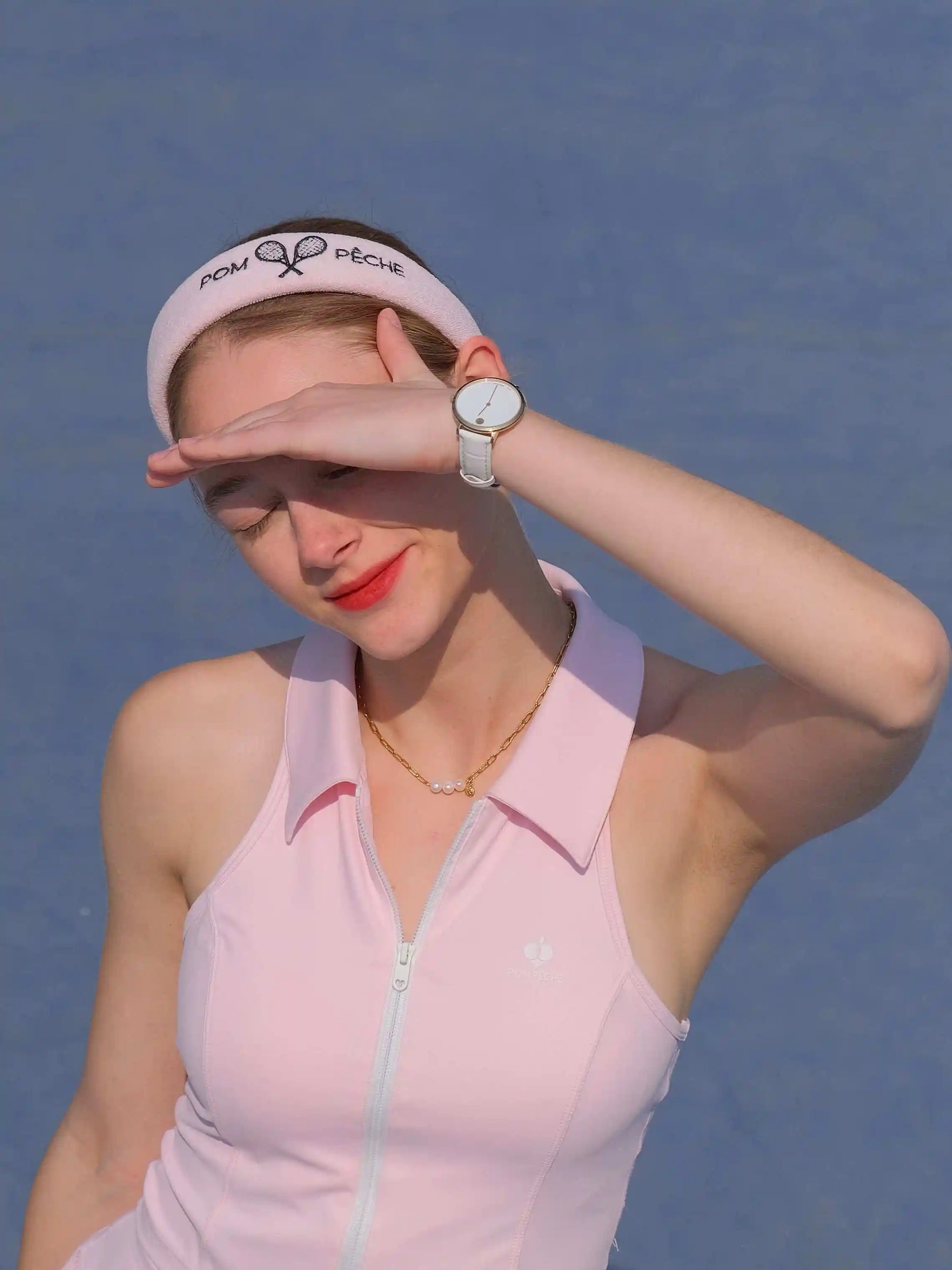 Woman in pink athletic outfit shielding eyes from sun with visor against blue background