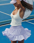 Woman in a white top and light purple tennis skirt on a blue tennis court.