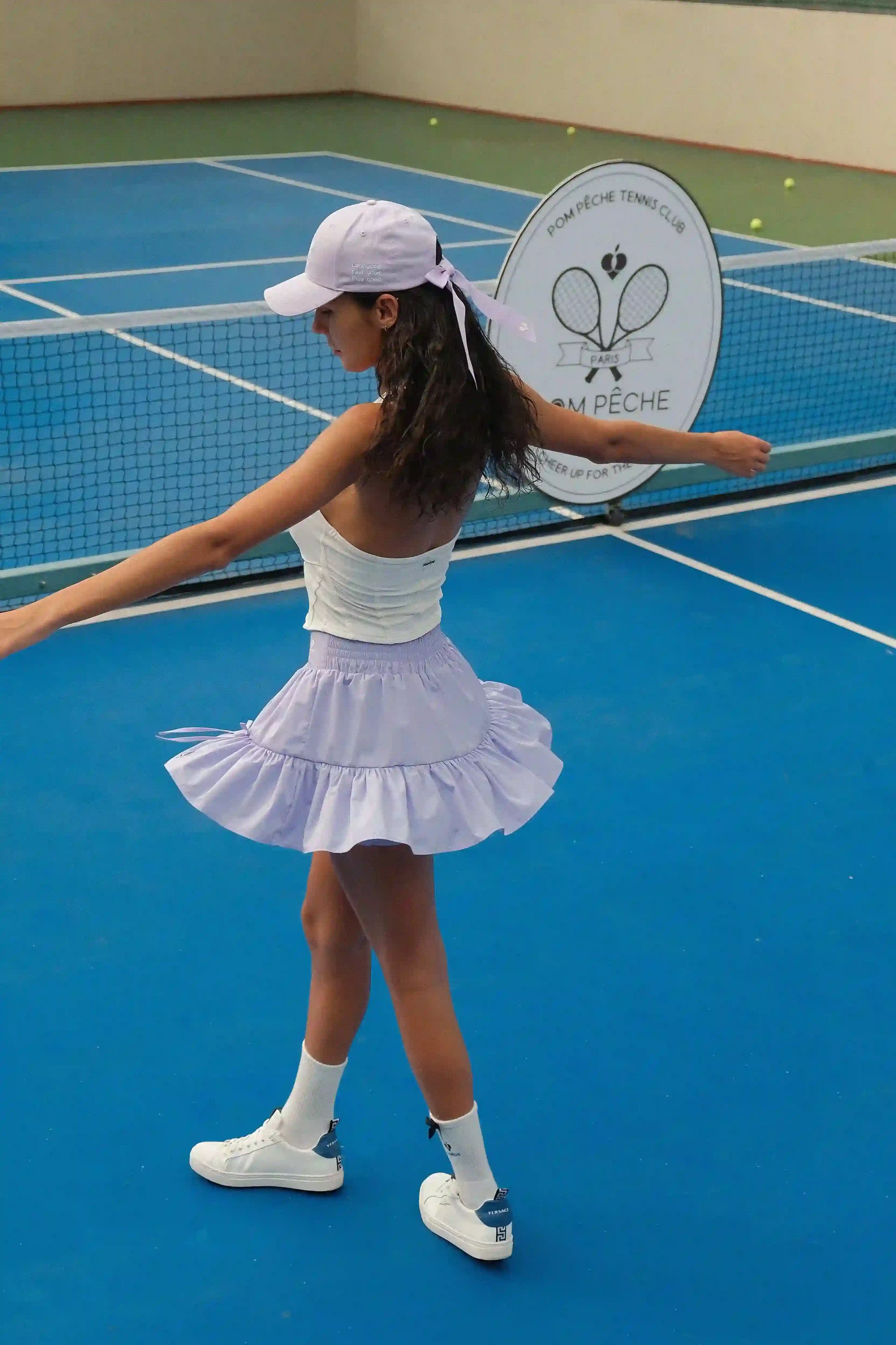 Woman in tennis attire on a blue tennis court with a club logo in the background
