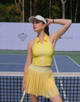Woman in yellow tennis outfit standing on a tennis court with trees in the background