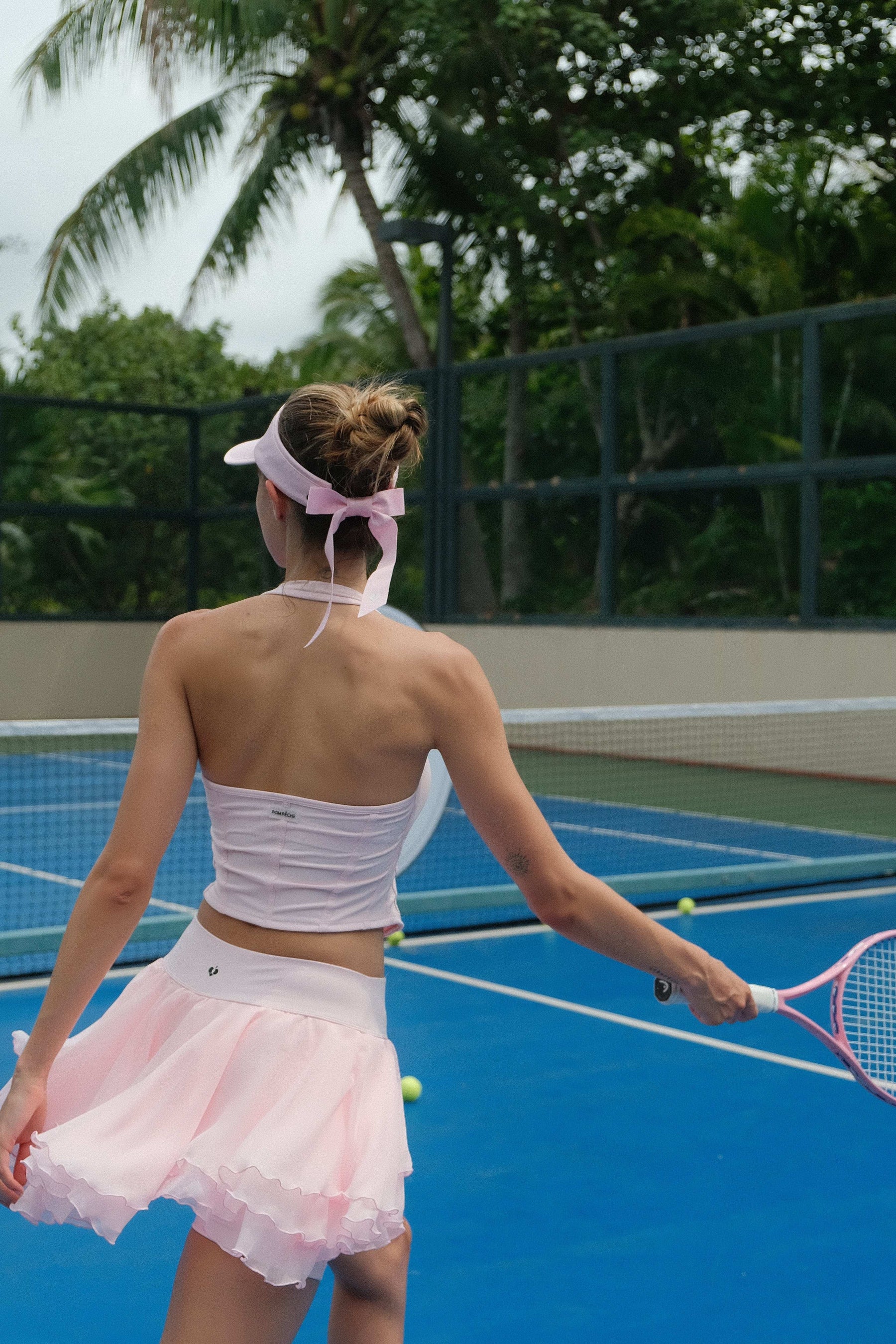 A woman prepares to swing her racket while wearing a pink ruffle tennis skirt on a blue court.